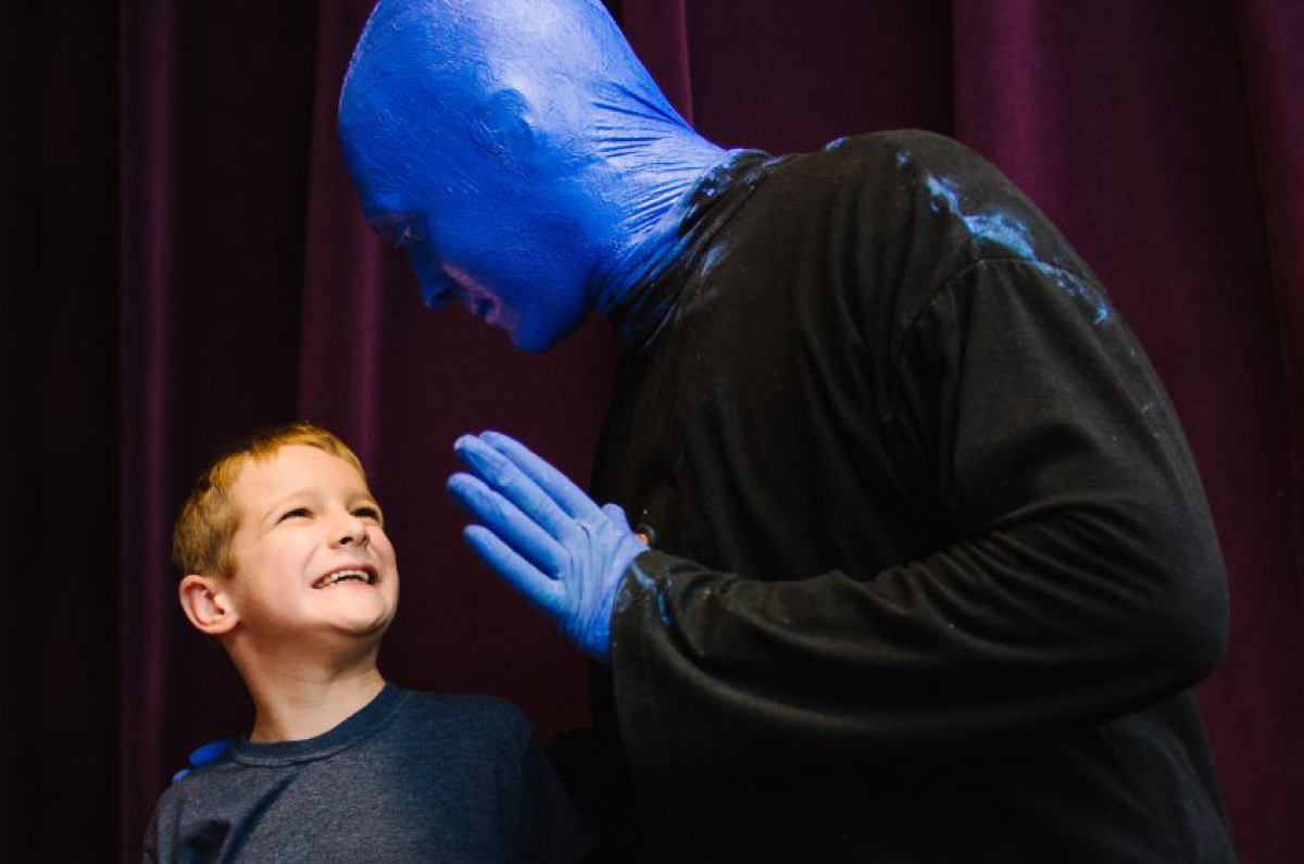 Blue Man Group member presents to a young boy with huge smile.